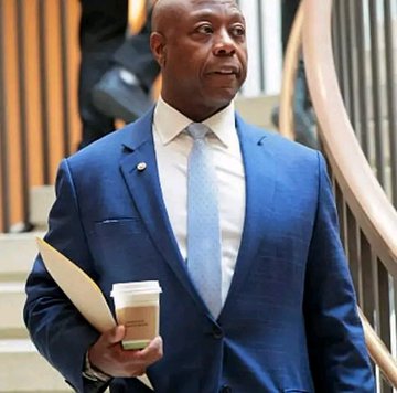 A man wearing a blue suit jacket walks down an indoor staircase while holding a coffee cup.