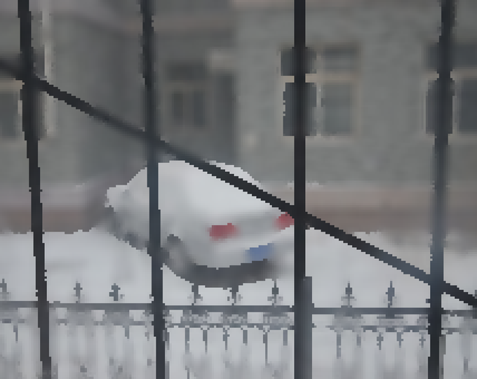A snowy car parked in front of a gray building, viewed through a metal fence with snow-covered tops, evokes a nostalgic winter scene shared as a limited pixel-art photography NFT piece.
