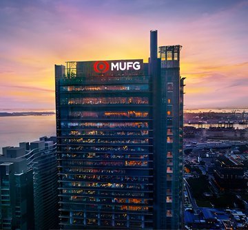 The MUFG (Mitsubishi UFJ Financial Group) headquarters building at sunset, with a bridge and cityscape visible across the water in the background.