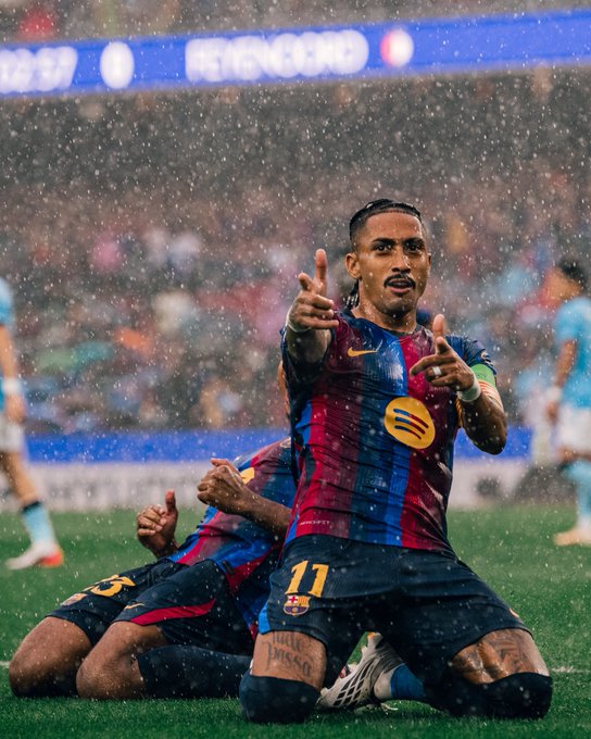 A Barcelona player (#11) celebrating on his knees in the rain during a match, with 'HEINEKEN' visible on a digital advertising board in the background.