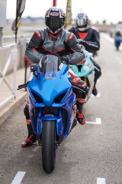 A motorcyclist in red, black, and white racing gear riding a blue sportbike on a track.