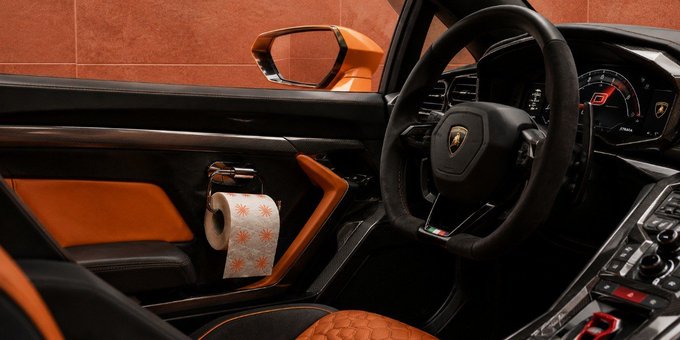 Interior of a Lamborghini featuring an orange and black color scheme with a roll of toilet paper hanging on the door.