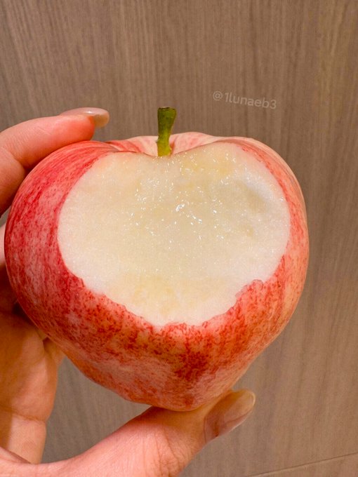 A hand holding a partially eaten red apple with a bite revealing the white flesh, with the watermark "©lunaeb3" visible.