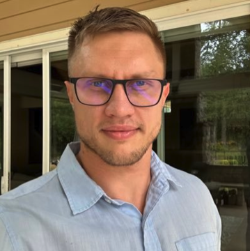 A man wearing glasses and a light blue button-up shirt stands outdoors on what appears to be a patio or porch area. The image likely depicts Roman Storm, the Tornado Cash developer referenced in the post about his retrial being scheduled for April 26, 2027.