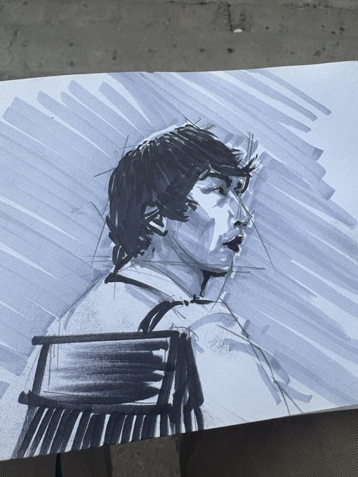 A quick gesture sketch in blue and black ink on paper, depicting a seated figure with dark hair looking to the right, with dynamic line work suggesting light rays in the background.