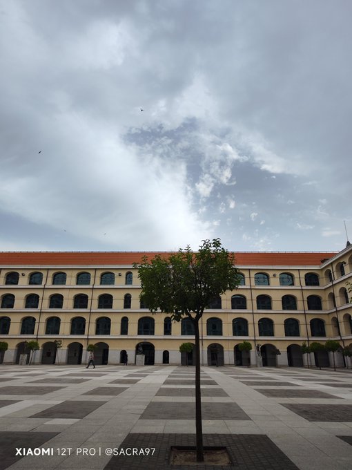 Photo of a large yellow historic building with arched windows surrounding a courtyard with a single tree, taken with a Xiaomi 12T Pro.