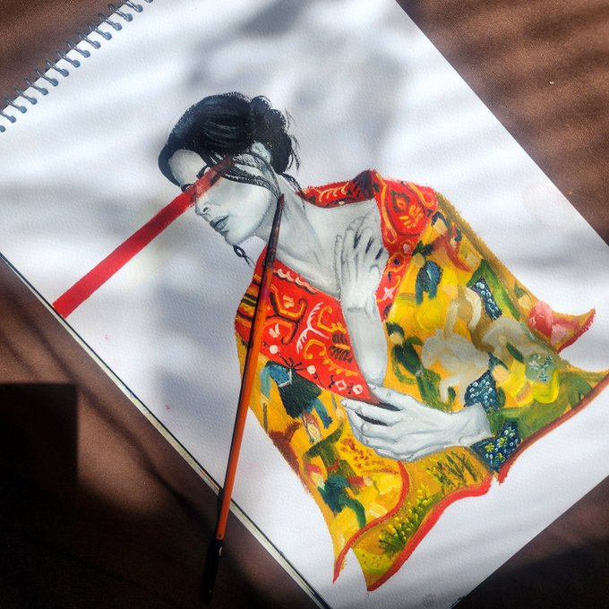 A watercolor painting in progress on a spiral-bound sketchbook showing a woman with dark hair wearing a flowing red, yellow, and green garment, with a red paintbrush lying across the artwork.