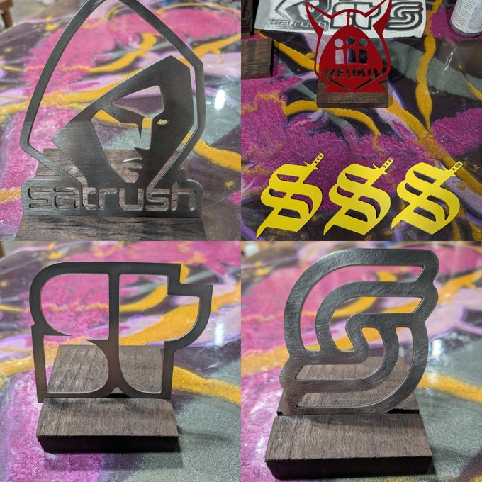 A four-panel collage showing laser-cut metal decorative pieces on wooden bases, including logos for 'SATRUSH', 'LI.FI', and a stylized 'S', with yellow lightning-bolt 'B' symbols overlaid on the top right.