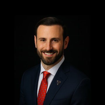 A professional headshot shows a smiling bearded man in a dark suit, white shirt, and red tie against a black background.