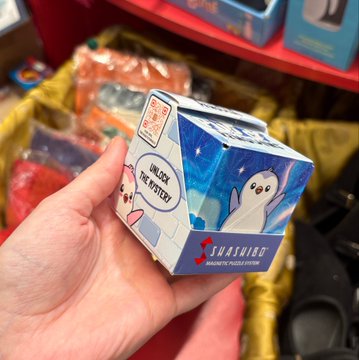 A hand holds a small decorative box labeled 'UNLOCK THE VICTORY' featuring illustrations of ghosts; the box is branded 'SHAWIBI' and described as an 'ORIGINAL TRADING STATION'.