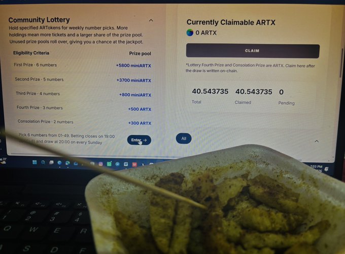 A laptop screen displaying a 'Community Lottery' interface for ARTX token prizes, showing 0 claimable ARTX and 40.543735 total/claimed, with a plastic container of food and a wooden skewer visible in the foreground.
