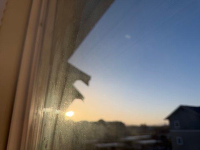The image features a window with a view of a blue sky, houses, trees, and power lines outside. The sun is shining brightly through the window, creating a warm glow inside the room. A caption below the photo reads "Good morning Doginal Dogs have a great day! Let's GOOOOOOOOOOO'". This message seems to be related to the image of the sunset or sunrise, as it suggests that the time of day could be either early in the morning or late at night when the sun is setting.

The caption also mentions dogs and houses, which might suggest a connection between the photo's content and the dog's name or the location where the house is located.