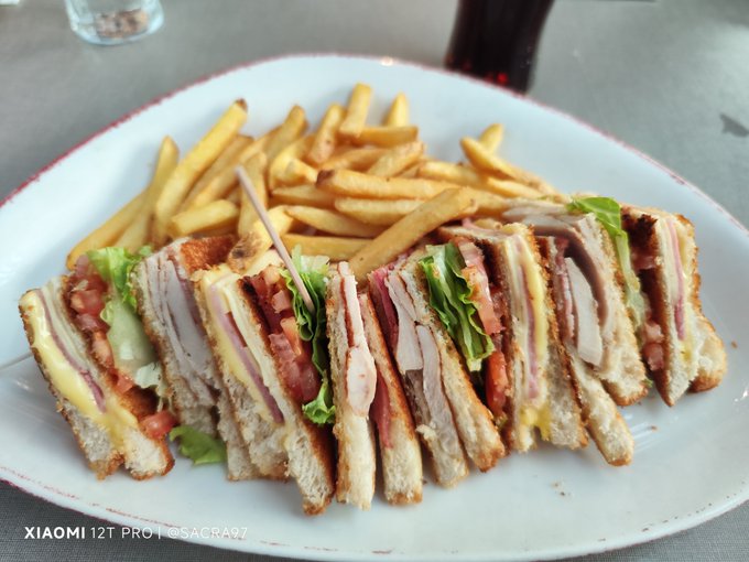 A club sandwich cut into multiple triangles, filled with ham, cheese, tomato, and lettuce, served alongside french fries on a white plate, photographed with a Xiaomi 12T Pro by @SACRA07.