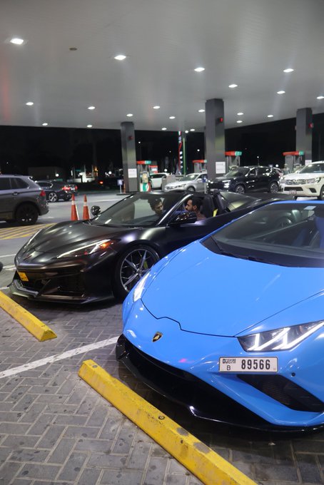 Two Lamborghinis—a black convertible with two occupants and a blue coupe with Dubai plate "D 89566"—are parked at a gas station under bright canopy lights. The image fits the "GN if you GN" caption by showcasing sleek, high-end supercars that would appeal to viewers who would acknowledge (or "GN") luxury car content.