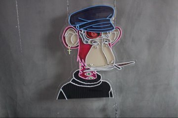 Photograph of a small embroidered or printed cartoon character patch on fabric, depicting a stylized figure in a police/military cap with red lips and exaggerated features in blue, red, and beige.