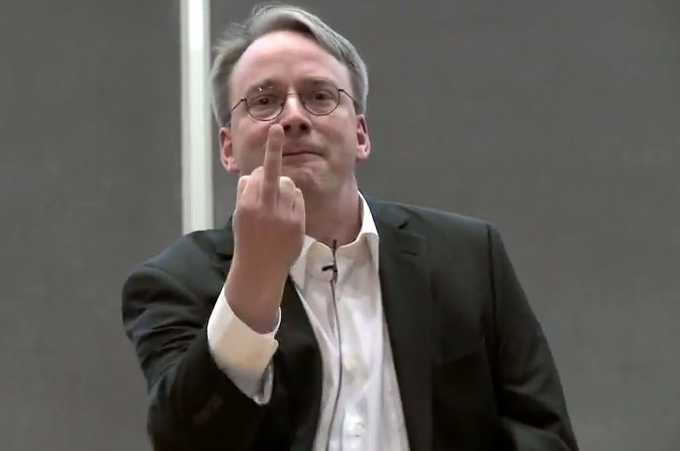A bespectacled man in a dark blazer and white shirt raises his middle finger directly toward the camera with a defiant expression. The image appears to be a reaction or humorous response to the post "Obscura on Linux at last!" — possibly expressing frustration or irreverent humor about the long-awaited news.