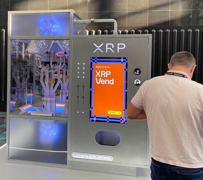 The image features a man standing next to a vending machine that says "XRP VEND" on its screen, with his hands on his hips as if he's about to make a purchase or enter some information into the machine. The background of the image is blurred and does not provide any additional context about the event taking place at the Permissionless conference.