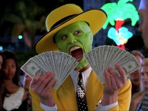 The Mask (Jim Carrey) wearing a yellow hat and suit, holding two fans of cash with his tongue out, set against a neon-lit night background.