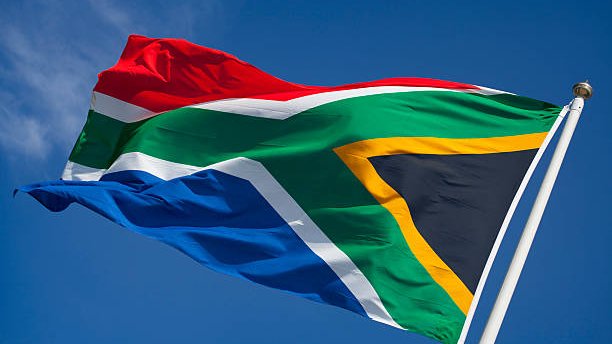 The South African flag waves against a clear blue sky.
