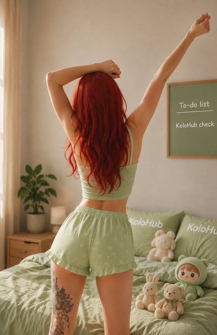 The image features a woman with red hair wearing green pajamas standing in front of a bed with teddy bears on it. She has her arms raised up in the air, suggesting that she might be feeling happy or excited about something. The photo also includes text elements such as "To Do List" and "Kolo Hub", which could possibly be related to the woman's morning routine or interests.