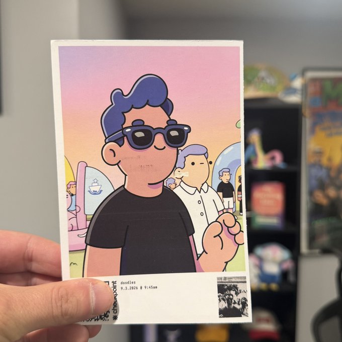 A hand holds up a printed card featuring a cartoon illustration of a person with purple hair and sunglasses, dated "9.3.2020 9:45am" with the word "doodles" visible.