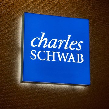 The image shows an illuminated Charles Schwab sign mounted on a textured wall. The sign relates directly to the post's announcement about the financial giant launching direct Bitcoin and Ethereum trading, representing the mainstream institutional backing referenced in the message.