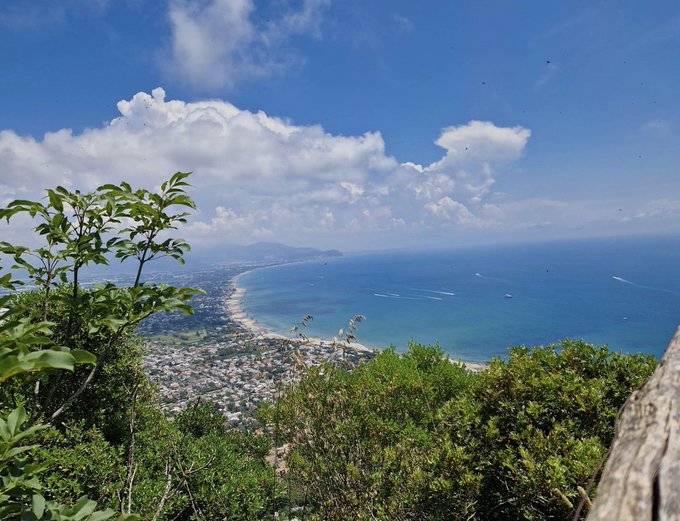 A breathtaking aerial view of a coastal city with a sweeping bay and lush green foliage in the foreground, likely taken from a scenic overlook—perfectly matching the post's vibe of a relaxing coastal getaway while reminding followers about sun protection, including the mention of "@SunscreenTech" being acquired by "fhenix."