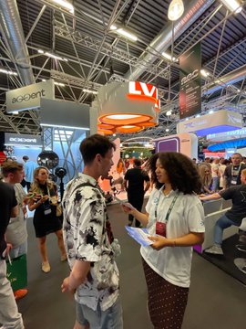 Busy indoor convention or exhibition hall with attendees, featuring an 'LVT' booth and an 'accvent' sign hanging from the ceiling, with people networking and walking around.
