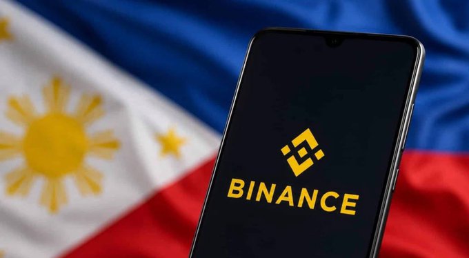 A smartphone displays the Binance logo in yellow against a background of the Philippine flag.