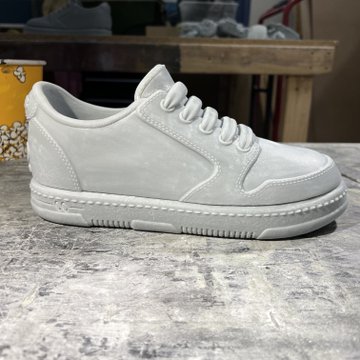 A pair of all-white low-top sneakers displayed on a concrete-textured surface, with a Popeyes cup visible in the background.