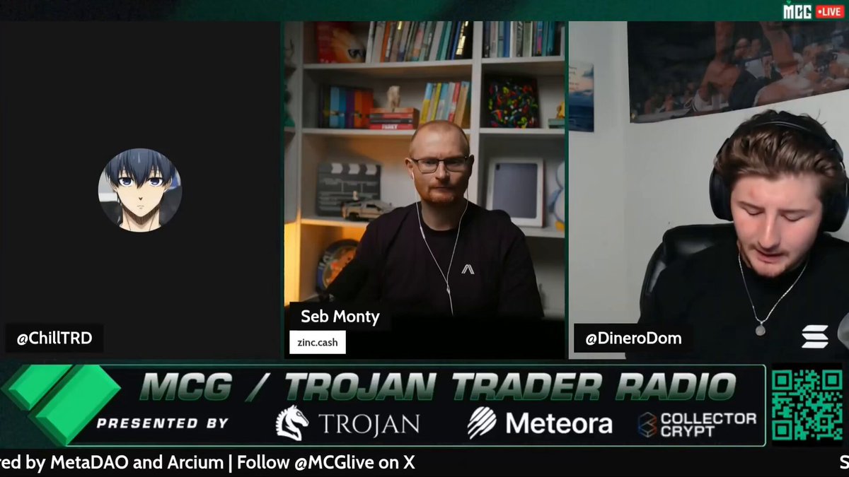 The image shows a man sitting behind a desk with a computer monitor displaying a video call from another person. The other person appears to be talking about cryptocurrency, specifically Solana's OG token (O2O). The man at the desk seems to be interested in what is being discussed and possibly considering investing or trading in this particular cryptocurrency.