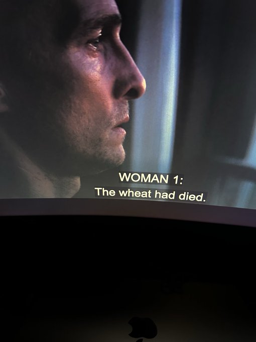 A close-up of a man's face in profile is shown on a screen with subtitles reading "WOMAN 1: The wheat had died," displayed above an Apple laptop logo.

The image relates to the streak by capturing a dramatic scene from the film "Arrival," which references the concept of time and continuity central to the streak's theme.