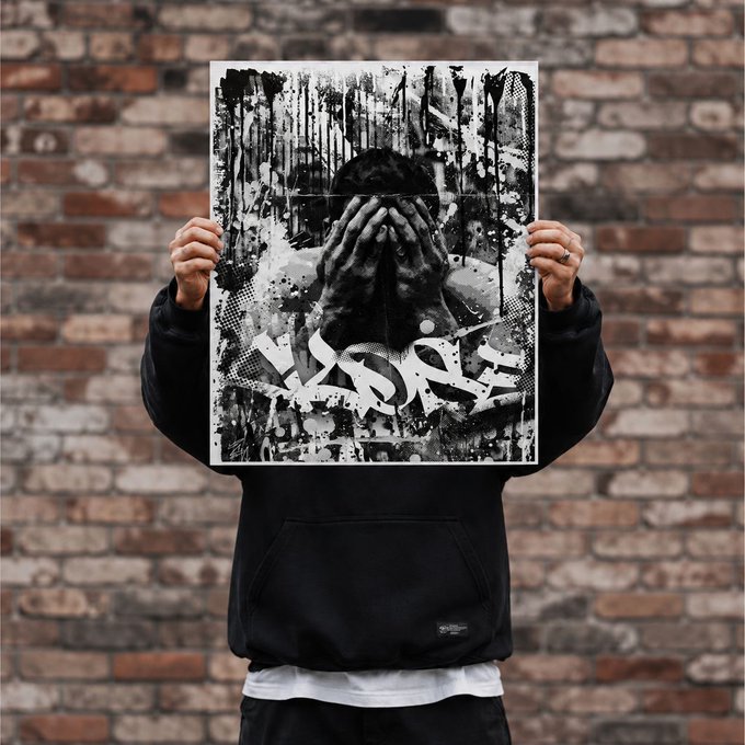 A person in a black hoodie holds up a black and white poster featuring a figure covering their face with their hands, set against a brick wall background.