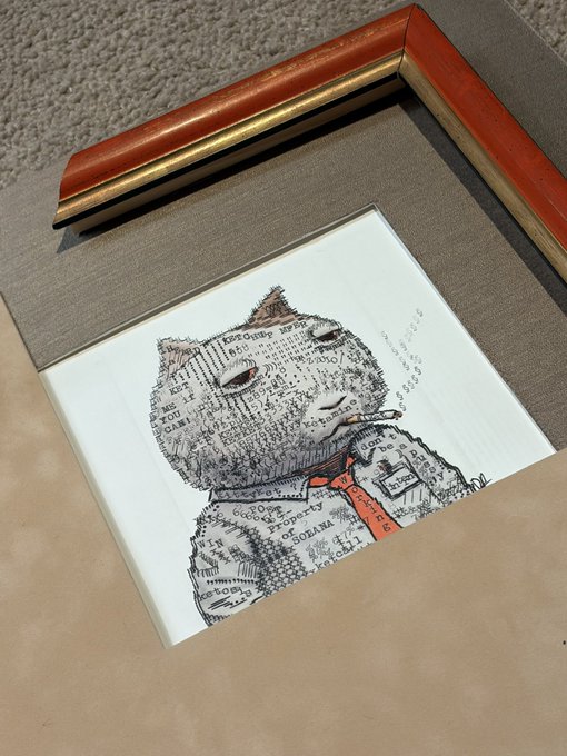 An artwork displayed beneath an empty picture frame, featuring a cat-like figure created from text fragments and words related to Africa, currency, and government, with a red tie, sitting on a brown surface.