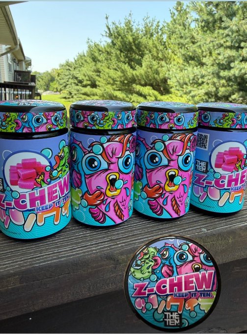 Several colorful, psychedelic-themed canisters of 'Z-Chew' branded product, with a cartoon dog character on the label and the tagline 'KEEP IT TEEN', displayed outdoors on a wooden table.