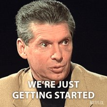 The image shows a man's face with his mouth open, showing surprise or excitement as he looks towards something outside of the frame. Below him, there is text that reads "We're Just Getting Started" in a combination of cursive and white font style, which appears at the bottom right corner of the photo on the image.