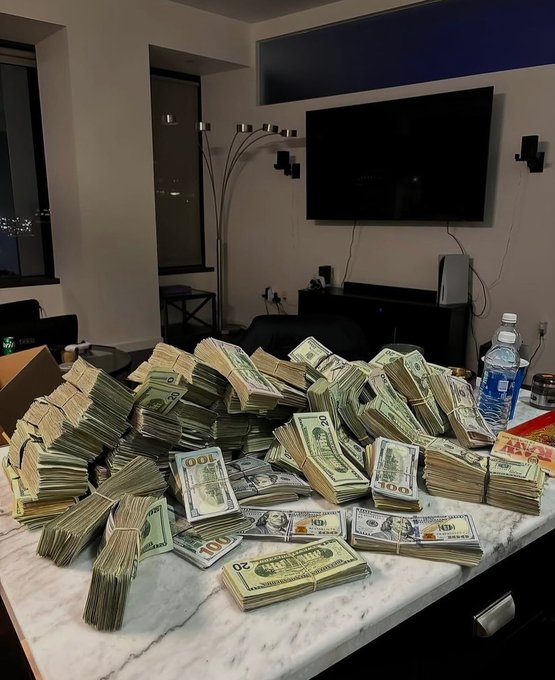 Large stacks and bundles of U.S. currency, including $100 and $50 bills, are piled high on a marble kitchen countertop in a modern apartment.