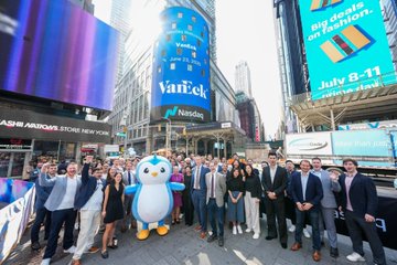 A group photo of the VanEck team standing in Times Square with the Nasdaq and VanEck buildings in the background, featuring a penguin mascot.