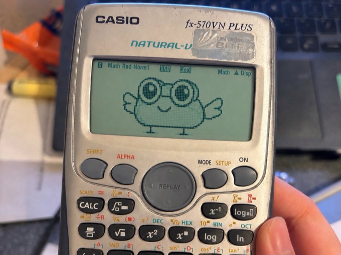 A Casio fx-570VN PLUS calculator displays a pixelated frog-like character with the text indicating the post ticker "$RWOG." The whimsical draw of the character's large, surprised eyes and open smile suggests a humorous, possibly ironic moment related to the ticker.