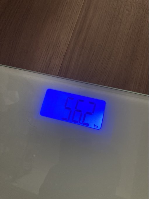 The image shows a scale with a blue digital display that reads "59.4 kg" and "58.8 kg". The scale is placed on top of a wooden table, which has a brown color.
