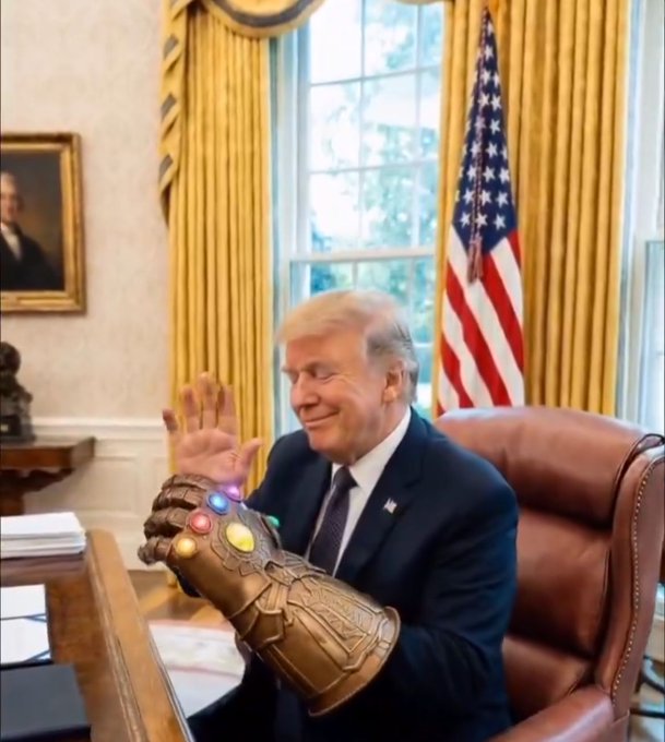An AI-generated image depicts a figure resembling Donald Trump sitting at the Resolute Desk in the Oval Office, wearing a suit and smiling while gesturing with a hand wearing Thanos's Infinity Gauntlet.