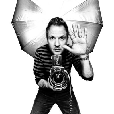 A man in a striped shirt poses dramatically behind a camera with a raised hand, set against a photographer's umbrella backdrop, evoking the imagery of someone actively capturing or soliciting content—fitting the post's playful request for BNB wallets tied to the "$Platon" token.