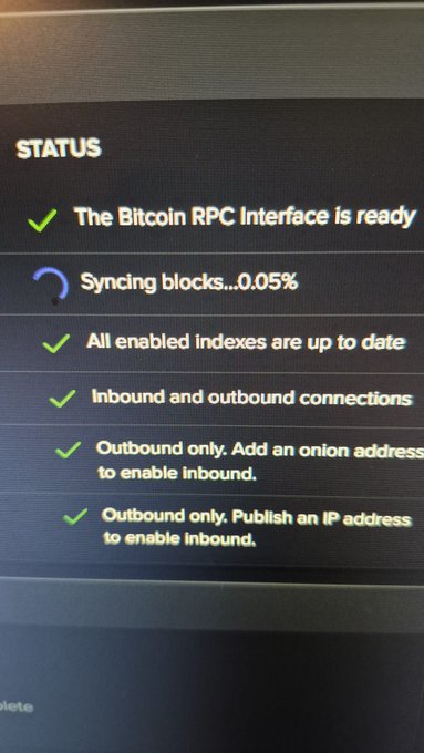 A monitor displays Bitcoin Core's status screen showing the RPC interface ready, indexes up to date, and the blockchain currently syncing from scratch at 0.05%, reflecting the user's return to Core and abandonment of the Knots fork.