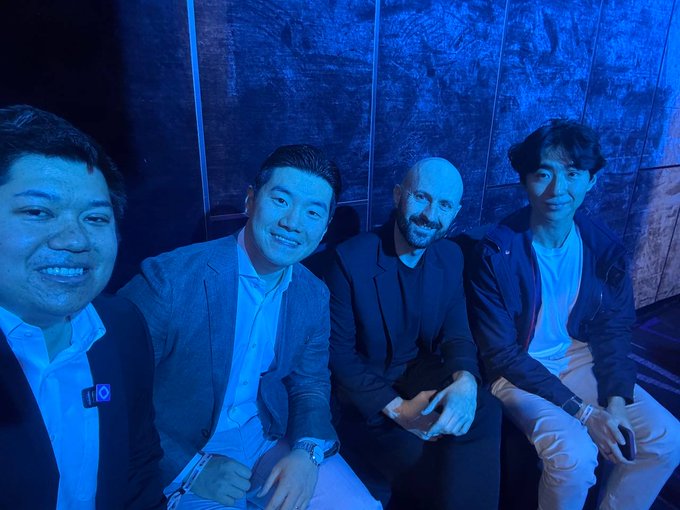 Four men pose together at an event, bathed in moody blue lighting, capturing a moment from a crypto/web3 gathering in Korea featuring representatives from Injective, Stellar, LayerZero, and Monad.