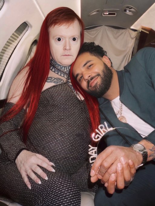 A photo of two people on a plane: a person with long red hair and facial piercings wearing a mesh top, sitting next to a smiling man with a beard wearing a dark jacket over a shirt that says 'DAY GIRL'.