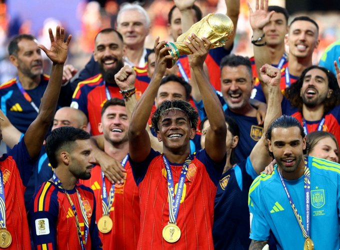 The image shows a jubilant team in red and blue jerseys celebrating a championship victory, with the central figure hoisting the FIFA World Cup trophy while wearing a gold medal. The image appears unrelated to the post, which announces "4lpha AI" as the "@0G_labs Zero Cup Champion" of a hackathon, with no visible connection to the World Cup celebration depicted.