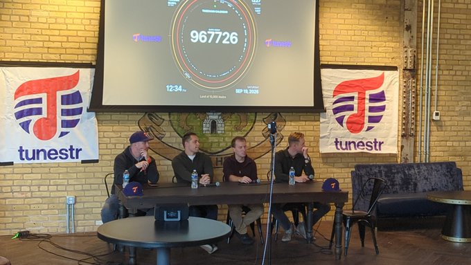Four men sit at a table during a panel discussion in front of a projection screen displaying '967726' and 'Last of 11,707 rolls' dated September 18, 2025, with 'tunestr' branding banners on either side.