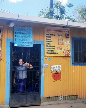 A photo of a small yellow food stand with a menu listing tacos, burritos, flautas, and other Mexican food items, with a person visible behind the barred entrance door.