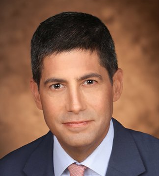 A professional headshot of a man with dark hair wearing a navy blue suit, white shirt, and patterned tie against a warm brown backdrop, accompanying a post about former Federal Reserve Governor Kevin Warsh's scheduled speech at the Jackson Hole economic symposium at 10 AM ET.