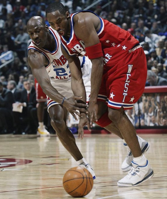 NBA players Moses Malone (#2) in a Philadelphia 76ers white jersey and J.R. Reid (#34) in a red Western All-Star jersey compete for a loose ball during the game.